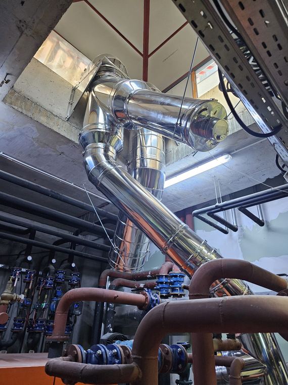 Tubulatură de exhaustare din inox cu coturi, montată la plafonul unui spațiu tehnic