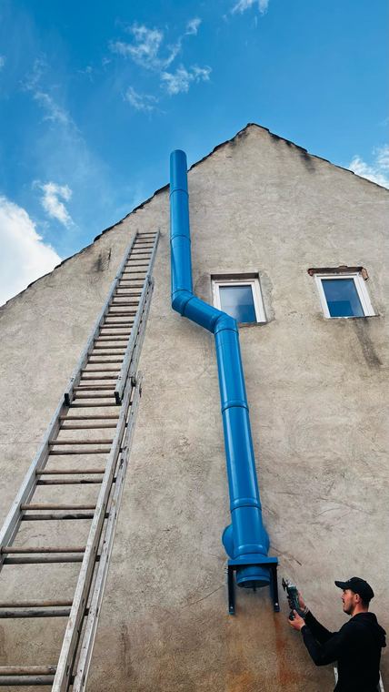 Tehnician montând traseul vertical al unui coș de fum pe peretele unei clădiri
