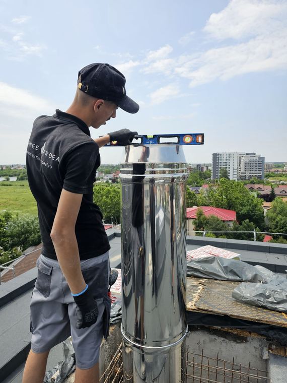 Tehnician verificând verticalitatea coșului de fum din inox cu nivela